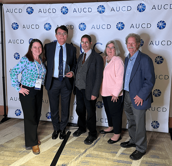 Kerim Munir (second from left) joined his colleagues, (L-R) Amy Szarkowski, Gyasi Burks-Abbott, Cindy Thomas and David Helm for photo after receiving his award. Kerim is holding the award and the group is standing in front of an AUCD background.