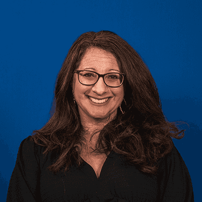 A white woman with dark hair, wearing glasses.