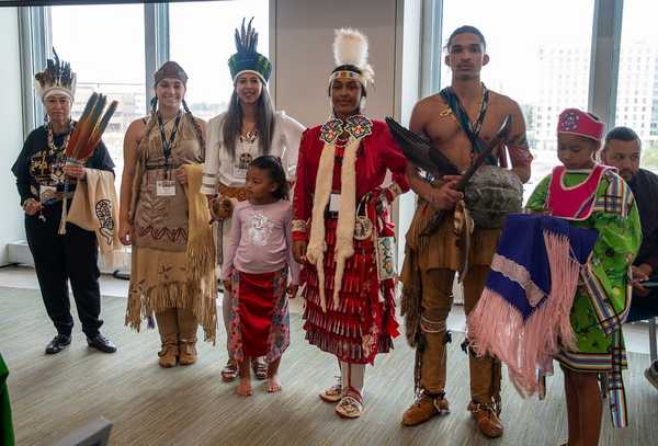 Four Indigenous drummers, one holding a toddler, drum and sing as traditional dancers performed.